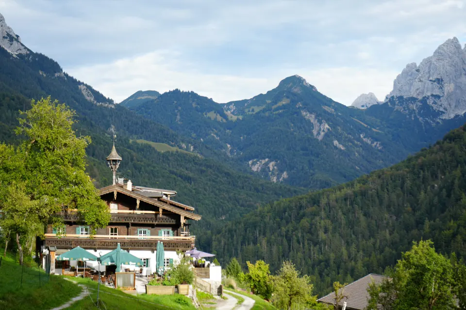 Berggasthof mit grünen Sonnenschirmen vor Bergpanorama