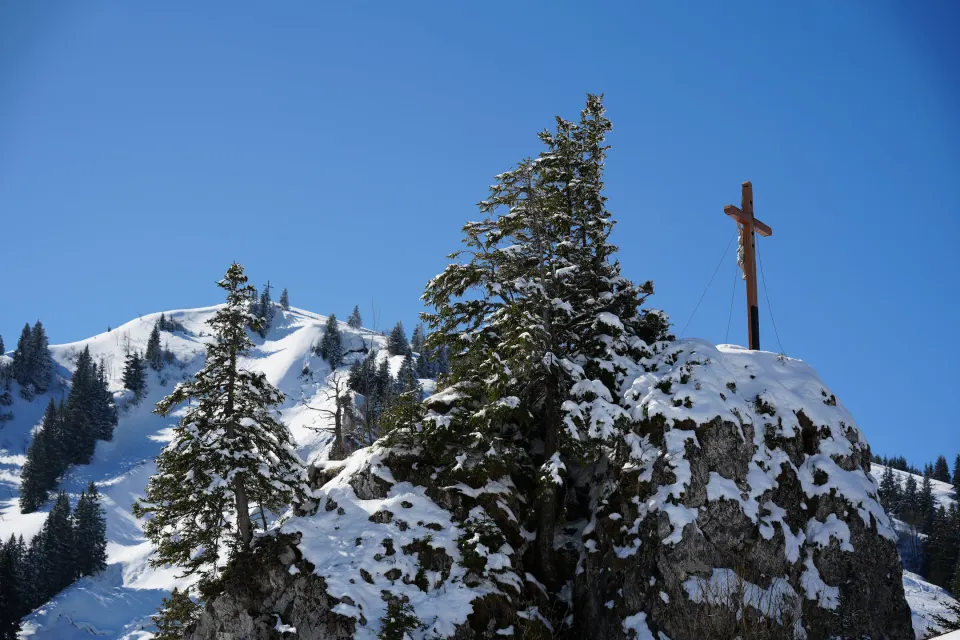 Gipfelkreuz zwischen verschneiten Fichten