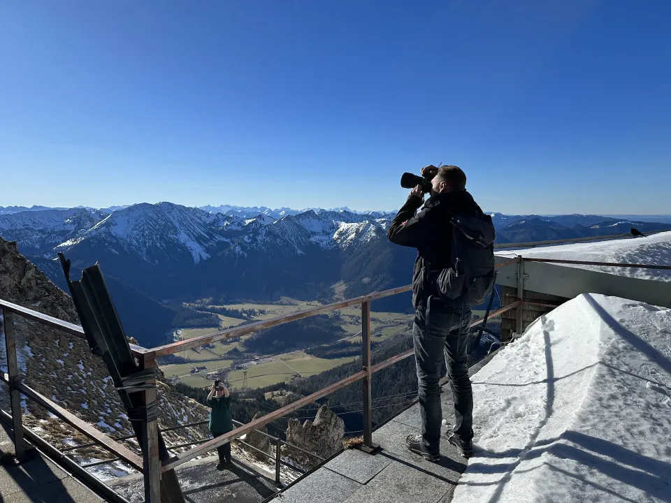Fotograf mit Kamera am Aussichtspunkt über einem Alpental